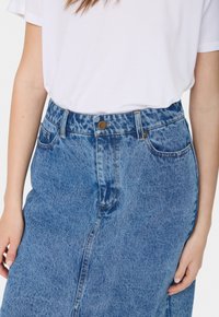 Világoskék farmer szoknya, enyhén elhalványított felülettel, magas derékú, fémből készült gombos záródással és hagyományos zsebekkel, egyenes szabással.