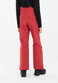 Pantaloni da esterno impermeabili rossi con bretelle nere regolabili, tasche laterali inclinato e vestibilità comoda, caratterizzati da una texture liscia e elegante.