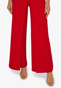 Červené kalhoty s širokými nohavicemi, hladkou texturou a rozděleným designem, doplněné o nahé skloubené sandály. Tkanina vypadá lehce a splývavě.