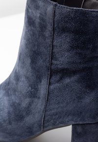 Botín de ante azul marino con una textura suave y lisa, que presenta una silueta elegante y detalles de costura a lo largo del lado.
