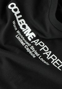 Svart t-skjorte av bomull med hvit tekst: "COLLECTIVE APPAREL Worn Worldwide© Styled Locally Limited Capsule." Enkel rund hals.