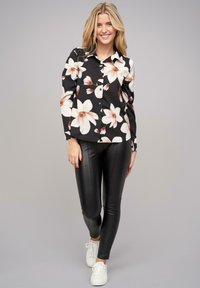 Zwarte bloes met grote witte en roze bloemen, lange mouwen, knopen aan de voorkant; gecombineerd met zwarte leren leggings en witte sneakers.