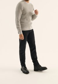 Szary sweter prążkowany z okrągłym dekoltem, zestawiony z czarnymi, dopasowanymi dżinsami i czarnymi sznurowanymi butami, na neutralnym tle.