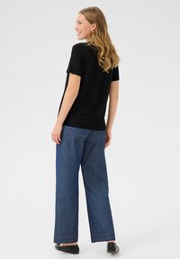 Sort kortærmet skjorte parret med brede blå denimbukser. Glat stof med en afslappet pasform, der viser en afslappet stil. Sorte sko synlige.