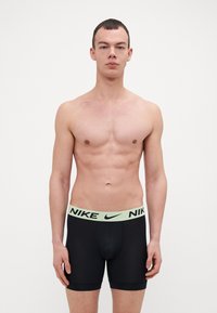 Črne bokserice z svetlo zelenim elastičnim pasom z logotipom "NIKE" v črni barvi. Material se zdi gladek in raztegljiv.