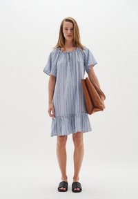Sininen ja valkoinen raidallinen mekko, jossa on leveät hihat, rypytetty helma ja nappiyksityiskohtia. Malli pitää ruskeaa laukkuolaa ja käyttää mustia liukupohjakenkiä.