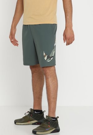 Mann trägt grau-grüne Sportshorts mit einem Tarnmuster-Nike-Swoosh und olivgrünen Nike-Sneakern mit schwarzen Socken.
