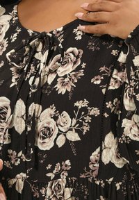 Abito nero a fiori con rose beige, dettagli con bottoni e un nodo sul collo. Tessuto testurizzato con orlo arricciato e maniche a sbuffo.