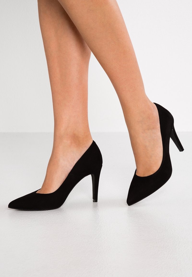 Tacones altos de ante negros con puntera afilada y un tacón stiletto moderado. Presentan una textura suave y un diseño clásico.