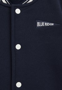 Marinblå sweatshirt med vita knappar, featuring en strukturerad tyg, och en broderad "BLUE RIDGE" etikett på en triangulär tygbit.