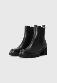 Bottines en cuir noir avec un large talon bloc, panneaux latéraux élastiques et fermeture éclair. Fini lisse et semelle en caoutchouc robuste.