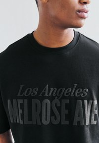 Crna pamučna majica s printom "Los Angeles MELROSE AVE" u raznim nijansama sive. Okrugli izrez, kratki rukavi, standardni kroj.