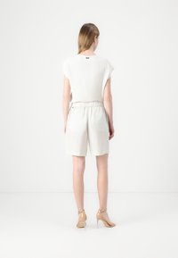 Hvit kortermet topp kombinert med lys beige shorts med elastisk midje og lommer. Modellen har på seg sko med gjennomsiktig hæl.