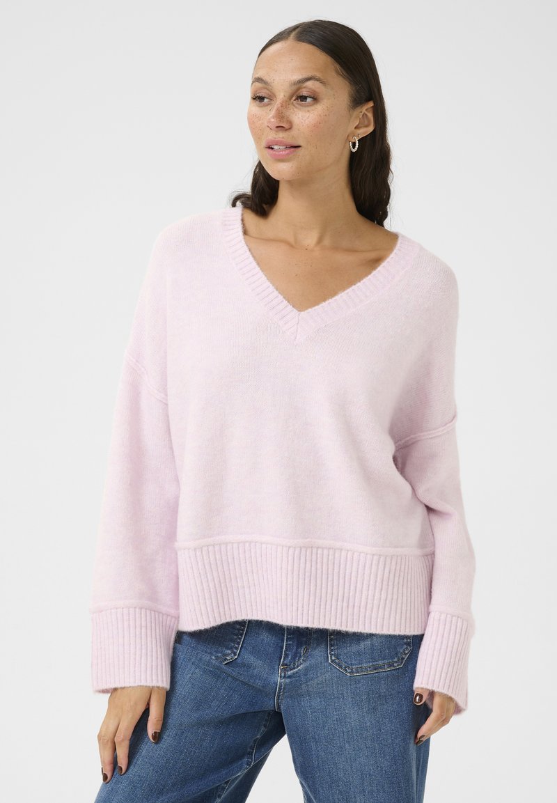 Maglione oversize di colore rosa chiaro lavorato a maglia con scollo a V, orlo e polsini a costine. Morbido al tatto, vestibilità rilassata, abbinato a jeans blu per un look informale.