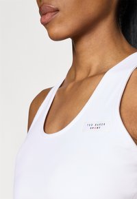 Balta sportinė marškinėliai su apvaliu iškirpimu, papuošti maža etikete su užrašu "TED BAKER SPORT", pagaminti iš lygaus, tampraus audinio.