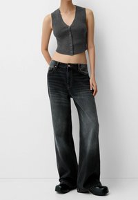 Grå randig kort topp med knappar, kombinerad med mörka vidbyxor och svarta träskor, vilket framhäver en avslappnad, modern klädstil.