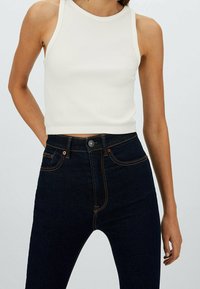 Vit ribbad crop-top kombinerad med mörkblå högmidjade jeans med orange sömmar och klassisk femfickdesign.