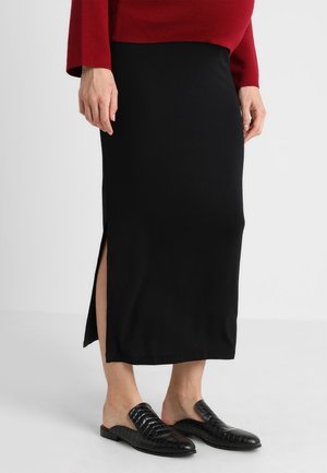 Frau trägt einen schwarzen Midi-Rock mit seitlichem Schlitz, roten Pullover und schwarze Slip-On-Flats mit strukturiertem Muster.