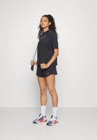 Juodas Nike marškinėliai su logo, derančios juodos šortai ir sportiniai batai su pilkais, baltais ir raudonais akcentais. Laikoma šokinimo virvė.