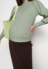 Zielony sweter prążkowany z bufiastymi rękawami, w połączeniu z brązową spódnicą prążkowaną. Stylową całość dopełnia torba z teksturowanego splotu z zielonymi akcentami.