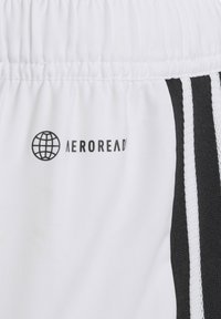 Shorts de sport blancs avec un logo noir et une ceinture texturée, dotés de rayures verticales noires et blanches sur un côté.