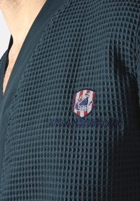 Navy blue bathrobe with a textured, waffle pattern and embroidered logo featuring a stylized bird on a shield. "JANVANDERSTORM" is also embroidered.