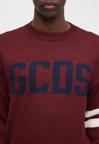 Bordowy sweter dzianinowy z dużym granatowym logo "GCDS", ribbowanym dekoldem oraz białymi i granatowymi paskami na rękawach.