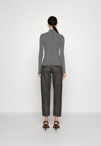 Top a maniche lunghe in bianco e nero a fantasia con colletto alto, abbinato a pantaloni dritti grigio scuro e sandali con tacco neri.