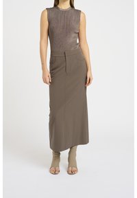 Débardeur en tricot marron sans manches associé à une longue jupe marron ajustée avec deux poches avant. Le mannequin porte des talons ouverts beige.