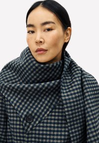Écharpe à carreaux dans des teintes bleu foncé et crème, dotée d'une texture douce, d'un grand col et d'un détail de bouton sur le devant.