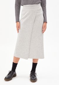 Gonna grigia fino al ginocchio realizzata in tessuto morbido con una vita in maglia, caratterizzata da un design avvolgente e una superficie liscia. Abbinata a scarpe nere e calze.
