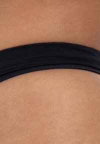 Schwarzes Gummiband, das über glatte Haut positioniert ist; hebt die Materialtextur und den Farbkontrast zwischen Stoff und Haut hervor.