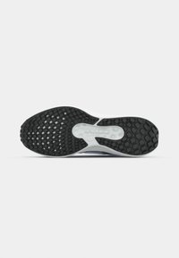 Semelle de chaussure avec bande de roulement en caoutchouc noir et section médiane blanche comportant un coussin d'air transparent et un grip à motif.