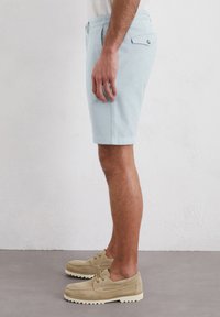 Shorts bleu clair en tissu texturé, présentant une coupe classique, des poches latérales et une poche arrière avec fermeture à bouton.