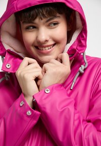 Jachetă waterproof de un roz strălucitor, cu o căptușeală pufoasă albă, glugă ajustabilă cu șnur și capse argintii la manșete. Textură netedă și lucioasă.