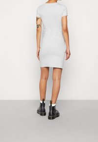 Szara, dopasowana sukienka t-shirtowa z krótkimi rękawami, sięgająca mid-thigh, o gładkiej fakturze. Noszona z czarnymi botkami za kostkę z kontrastowym przeszyciem i zamkami błyskawicznymi.