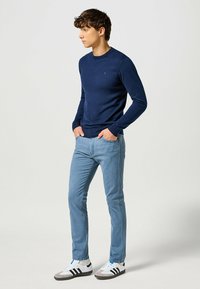 Maglione a maniche lunghe di colore navy abbinato a jeans blu chiaro e sneakers bianche con strisce nere. Il maglione ha un collo a giro.
