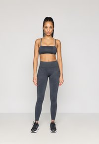 Σκούρος γκρίζος αθλητικός στηθόδεσμος και κολάν σε μαλακό, ελαστικό ύφασμα. Τα κολάν έχουν ψηλή μέση, συνδυασμένα με μαύρα αθλητικά παπούτσια.