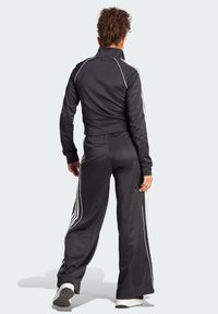 Black athletic tracksuit with long sleeves and pants, featuring white side stripes. Smooth, stretchy fabric, relaxed fit, and high collar.
