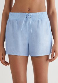 Lichtblauwe shorts met verticale witte strepen, elastische tailleband en een trekkoordsluiting. Zachte stof met een ontspannen pasvorm en zijsplitten.