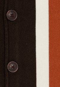 Randig tyg med svarta, vita och rostfärgade ränder, med en mörk knapp med fyra hål, strukturerat stickat material.