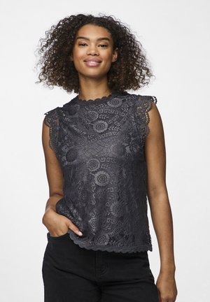 Top in pizzo grigio scuro con motivi floreali, bordi ondulati e maniche a cappuccio. Tessuto testurizzato, vestibilità relaxed. Indossato con pantaloni neri.