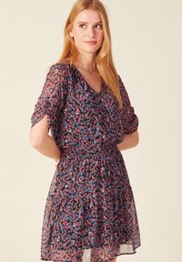 Blumenmusterkleid aus durchscheinendem schwarzem Stoff mit V-Ausschnitt, gerafftem Taillenbereich und kurzen Puffärmeln. Verfügt über bunt gemusterte kleine Blumen.