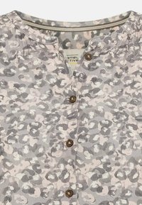 Knap-fra-bluse med leopardmønster i grå, beige og sort; har en rund halsudskæring og brune knapper langs fronten.
