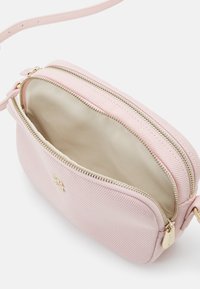 Borsa a tracolla in tessuto rosa con zip e ferramenta dorate. L'interno è di colore crema e presenta un compartimento principale con una texture morbida.
