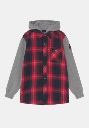 Chemise à manches longues à carreaux rouges et bleu marine avec capuche et manches grises, fermeture à boutons, poche poitrine et écusson rond sur le bras gauche.