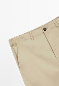 Beige cotton shorts with a button front, elastic waistband, and side pockets. Smooth texture with subtle stitching details.