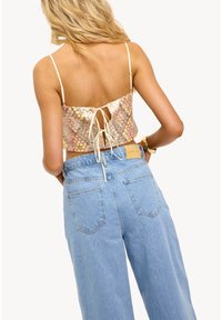 Pailleté crop top in pastelkleuren met een lace-up achterkant en dunne spaghettibandjes, gecombineerd met lichtblauwe high-waisted denim jeans met achterzakken.