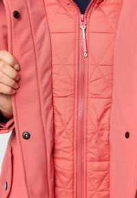 Pink waterproof jacket with a diamond-quilted inner lining and front zipper. Features snap buttons and a soft texture.