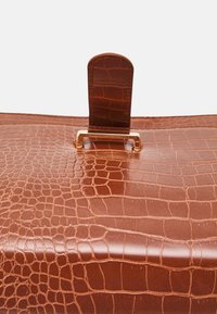 Brown crocodile-embossed leather bag with a gold-tone metallic clasp and tab closure. Smooth, glossy texture with defined patterning.